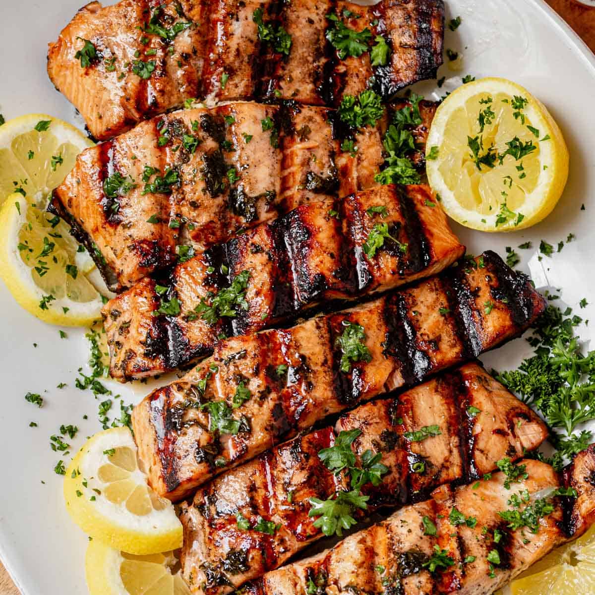Grilled salmon fillets with lemon slices and fresh herbs on a white platter
