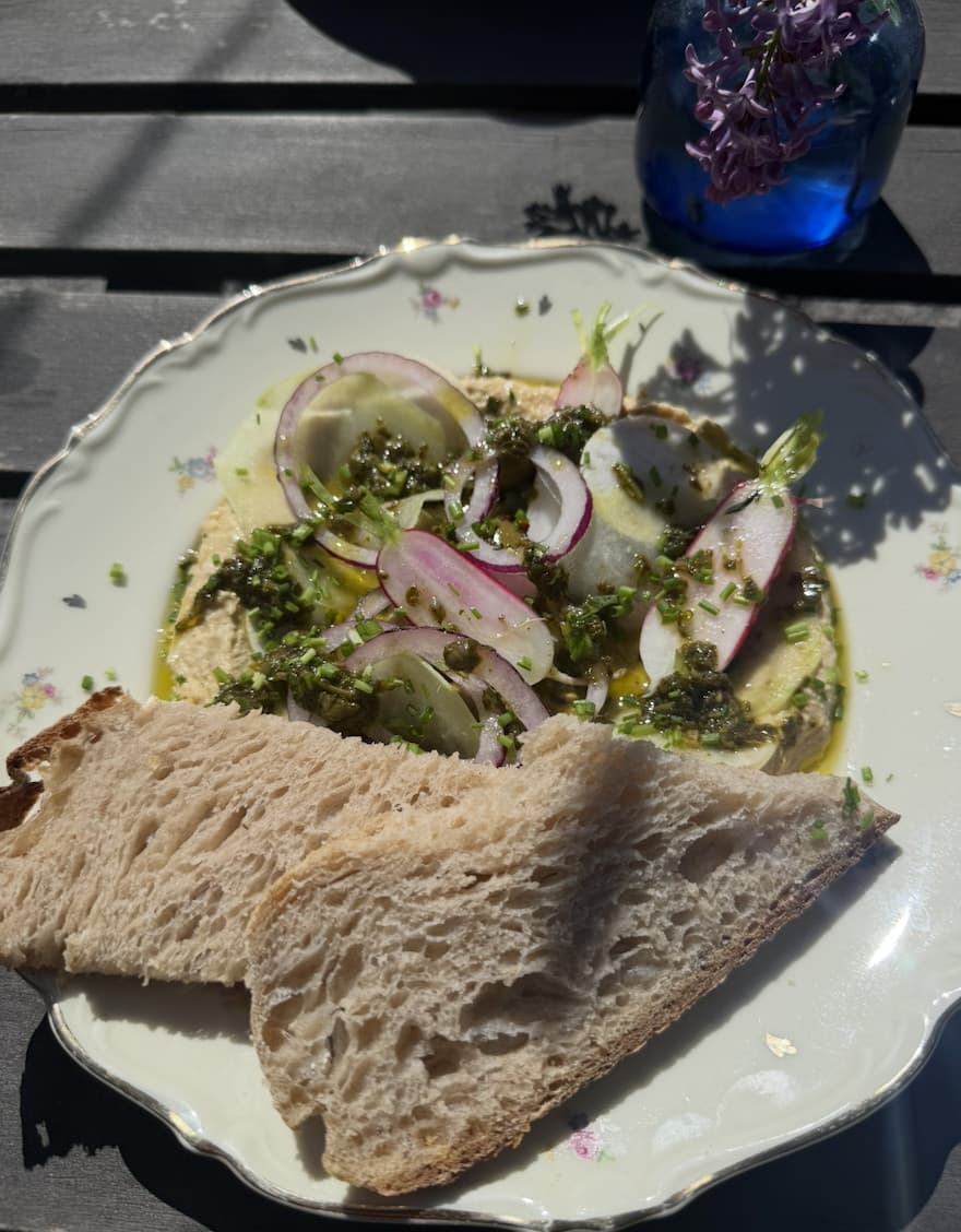 Hummus topped with salsa verde, shaved kohlrabi, radish, red onion and olives, served with sourdough on a vintage plate