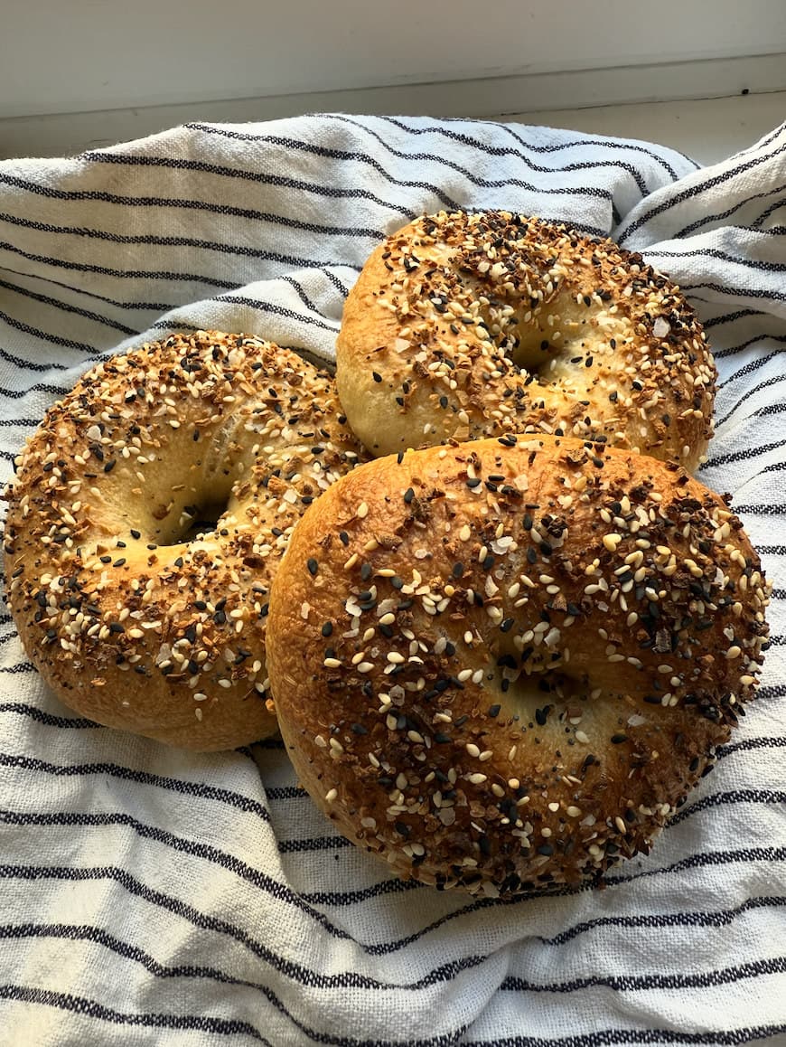 Three everything bagels piled on a striped linen cloth